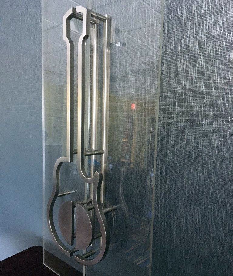 A photo of an architectural building product. Custom door handles designed in a guitar shape, displayed on a wall in a room.