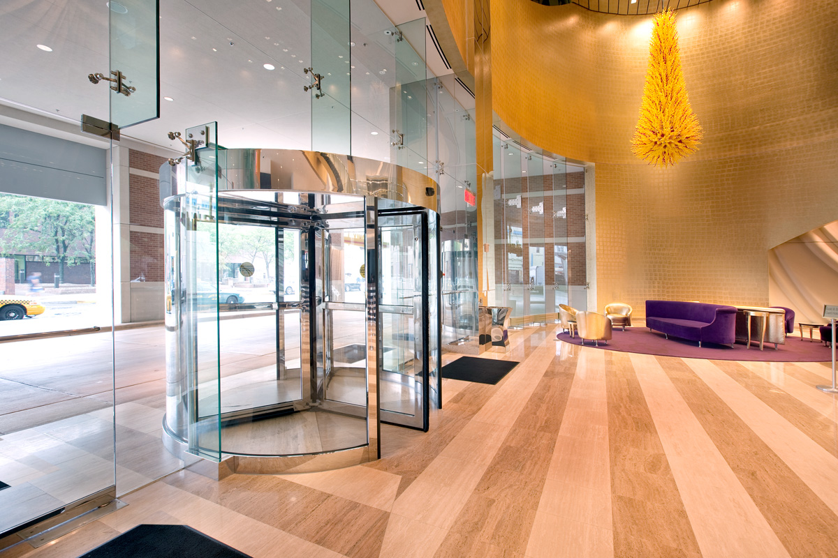 A photo of an architectural building product. An interior entrance to a large building, showing glass revolving doors and an upscale lobby.
