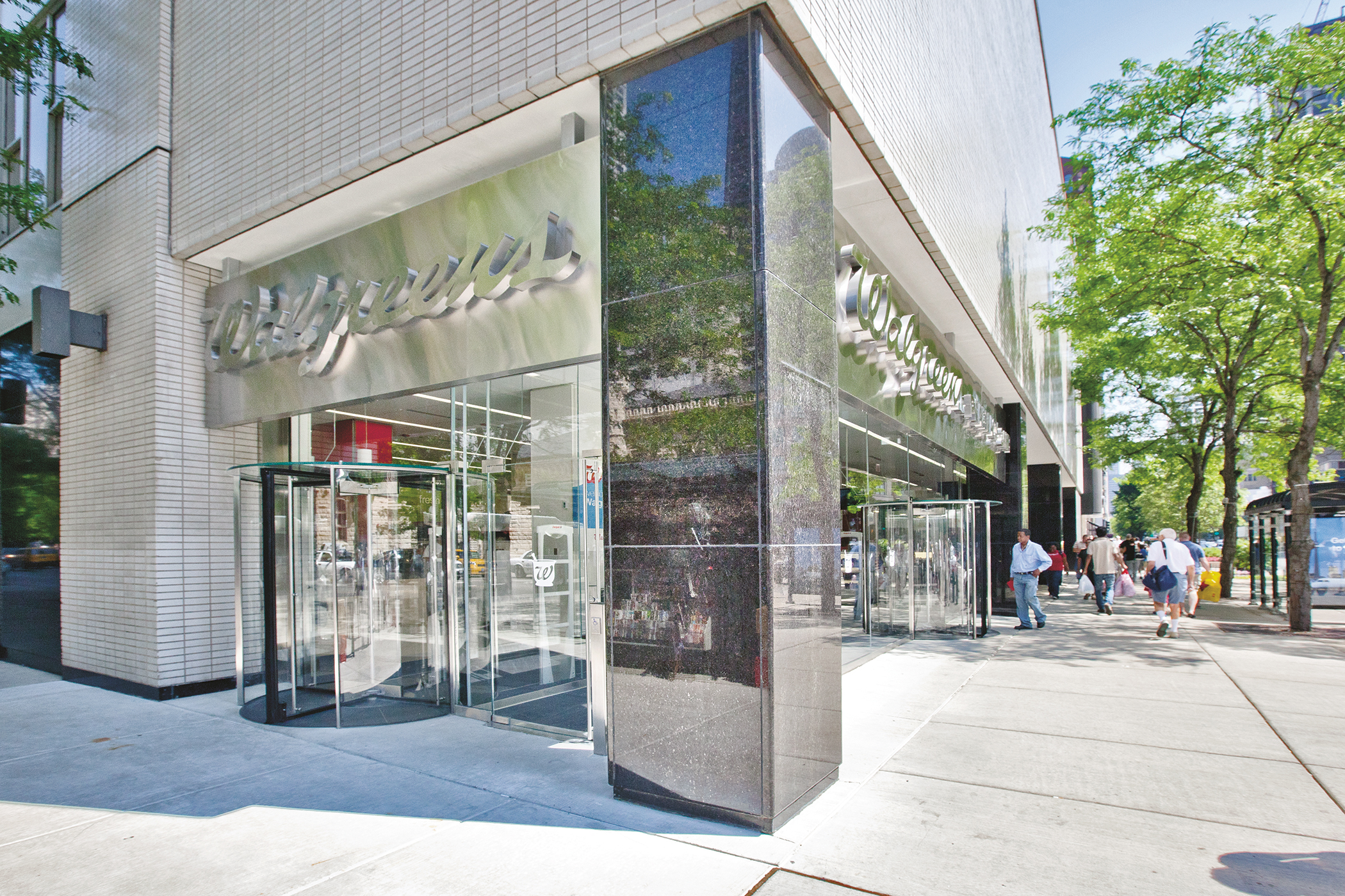 A photo of an architectural building product. An exterior entrance to a Walgreens pharmacy, at the base of a large building, showing glass revolving doors.