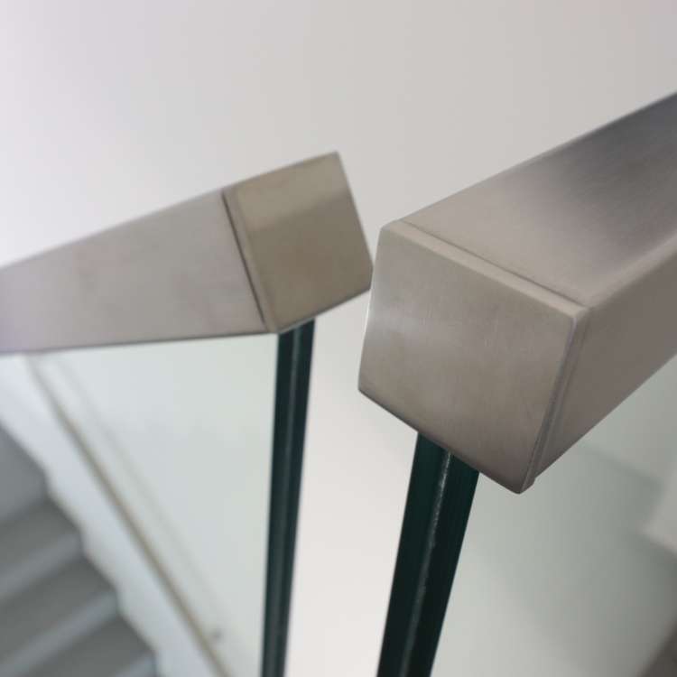A photo of an architectural building product. An interior detail image of a glass railing with a hand rail, beside a staircase.